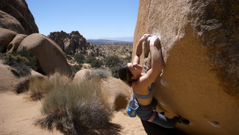 woman bouldering on large rock formation in a desert landscape