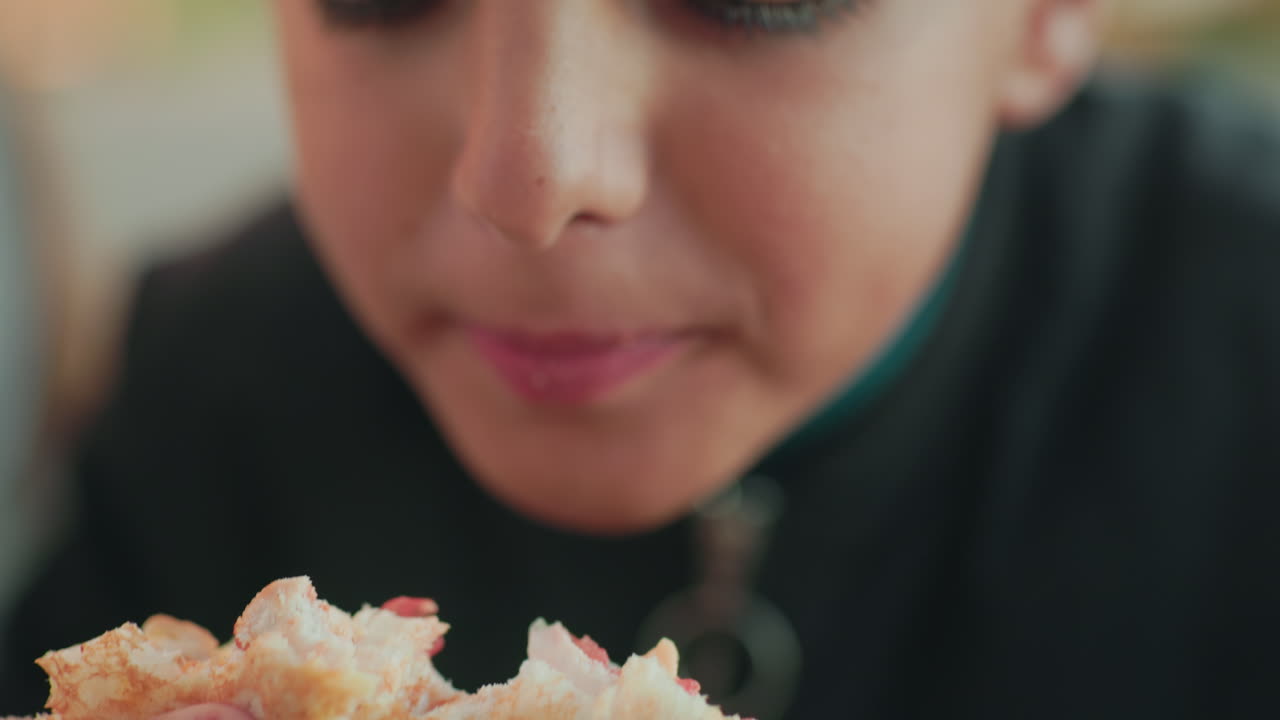 Close up kid savoring burger with both hands, mouth open ready to bite into fresh bread and filling, focus on detail of food and fingers, outdoor daylight scene with natural relaxed mood