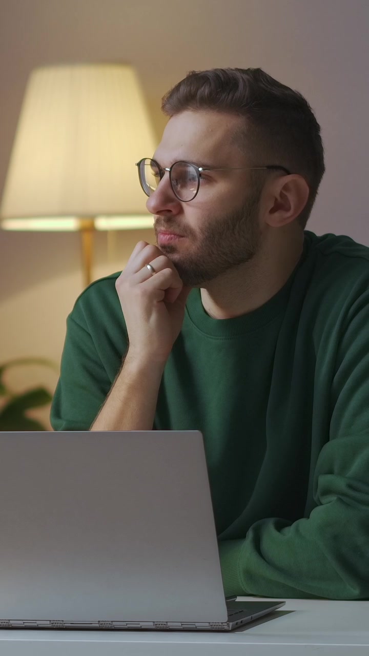 Thoughtful Young Man Working on Laptop at Home