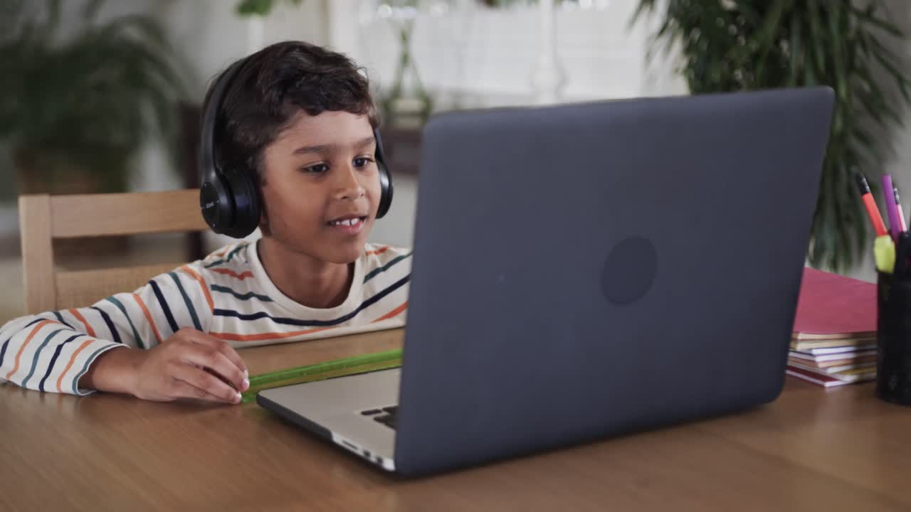 niño biracial aprendiendo en línea usando computadora portátil en la mesa, cámara lenta