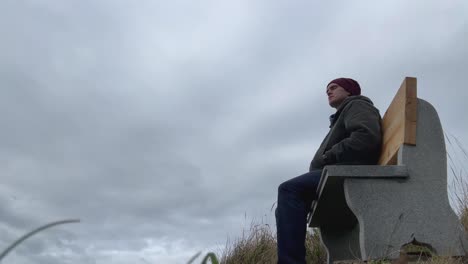 man looking afar sitting on the bench against cloudy sky