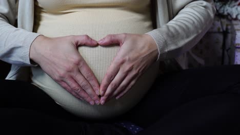 Pregnant-woman-hold-hands-in-heart-shape-near-twinkle-Christmas-lights