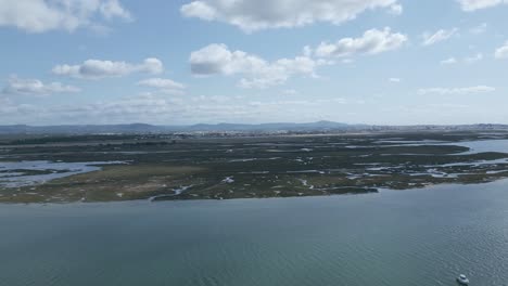 From-a-bird's-eye-perspective,-the-Ria-Formosa-stretches,-with-the-backdrop-of-Faro-in-Algarve,-Portugal,-creating-a-mesmerizing-aerial-footage