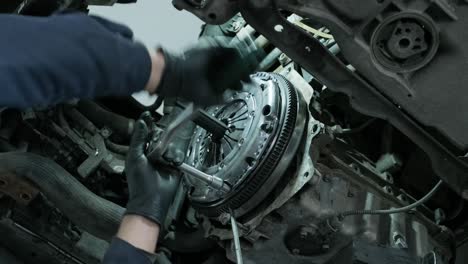 auto mechanic in protective working gloves, unscrews the clutch pressure plate under the car engine