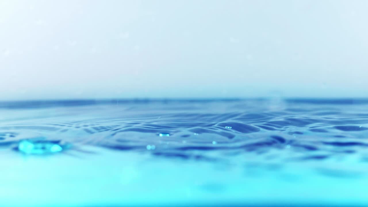 슬로우 모션의 깨끗한 물 표면은 물이 튀는 상점으로 화면을 채우고 기포로 액체 표면을 흔들고 있습니다.