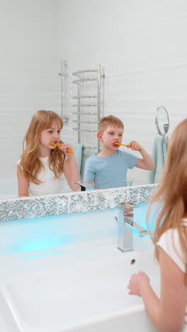 boy girl brushing teeth together in bathroom in front of mirror morning hygiene dental health care