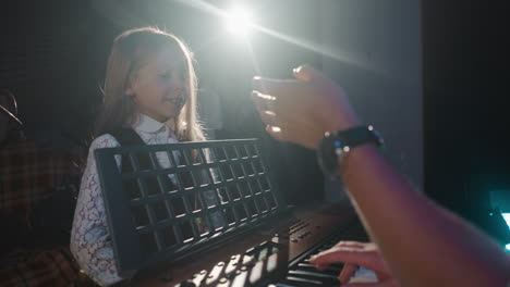 child grasps art of singing with educator. petite learner hones vocal skills with teacher at synthesizer against back light. artistic youngster