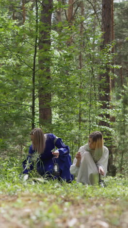 women in medieval costumes pick medicinal herbs on wood glade. witches gathers ingredients for poison. ancient traditions of healing at reconstruction