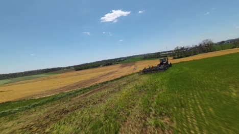 green farm fields and plowing machinery at work during sunny day in american countryside