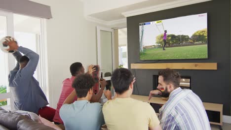 diverse friends supporting and watching tv with male soccer player playing match on screen