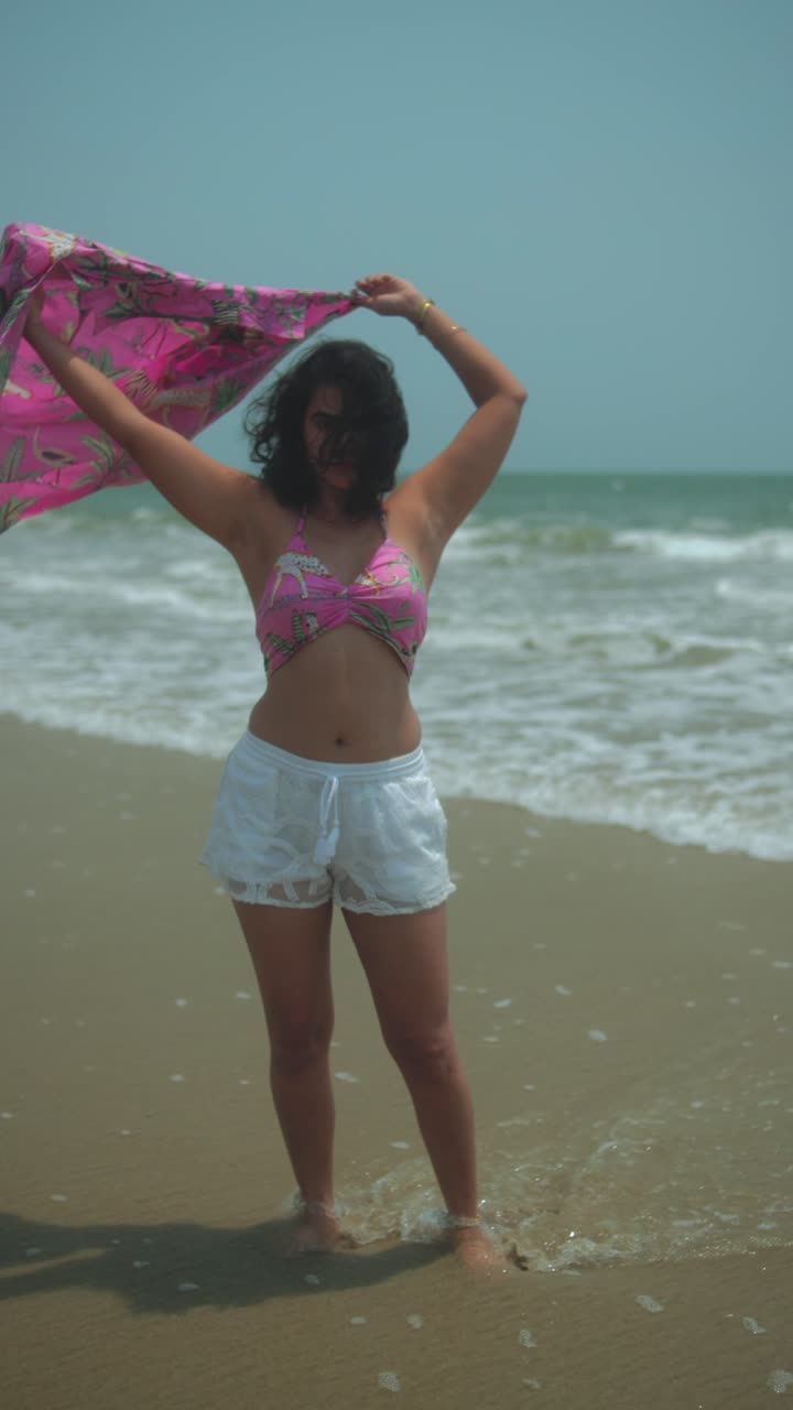 Woman enjoying ocean breeze, wearing pink shirt and white shorts on sunny beach