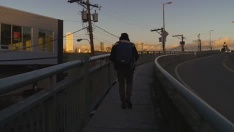 person walking on a bridge at sunset with city skyline in the background