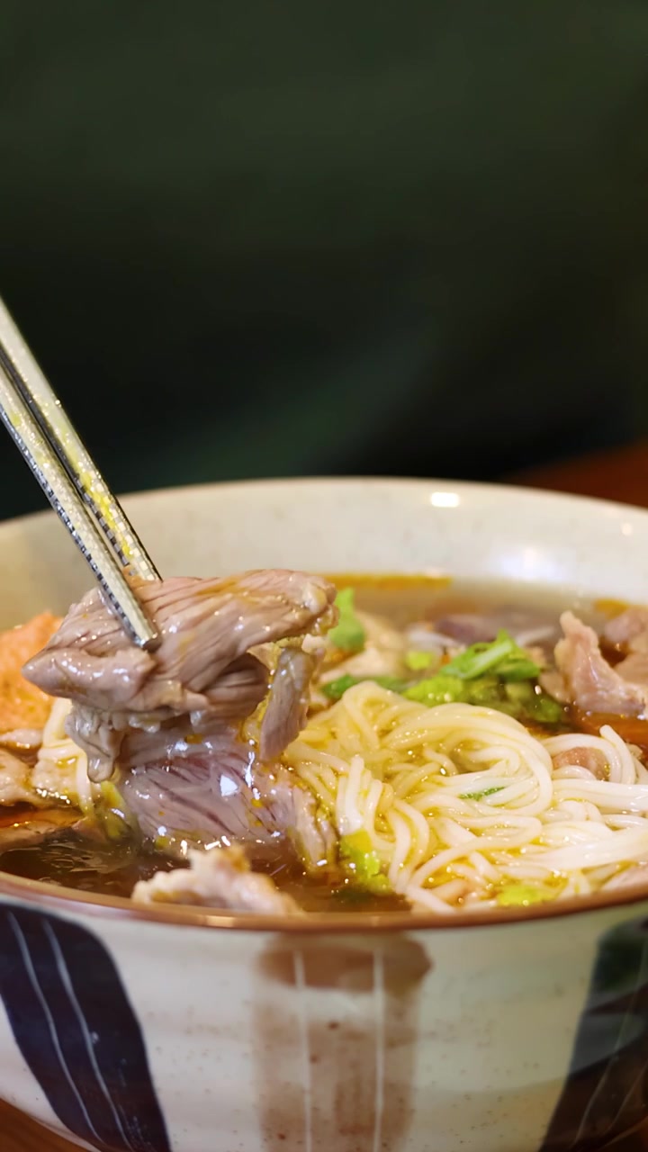 Đũa kim loại gắp những lát thịt bò mềm từ một bát phở truyền thống Việt Nam đang bốc khói