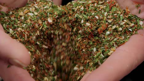 extreme close up of woman hands dripping delicious spices with basil, pepper, garlic, paprika, chili and parsley against black background in slow motion