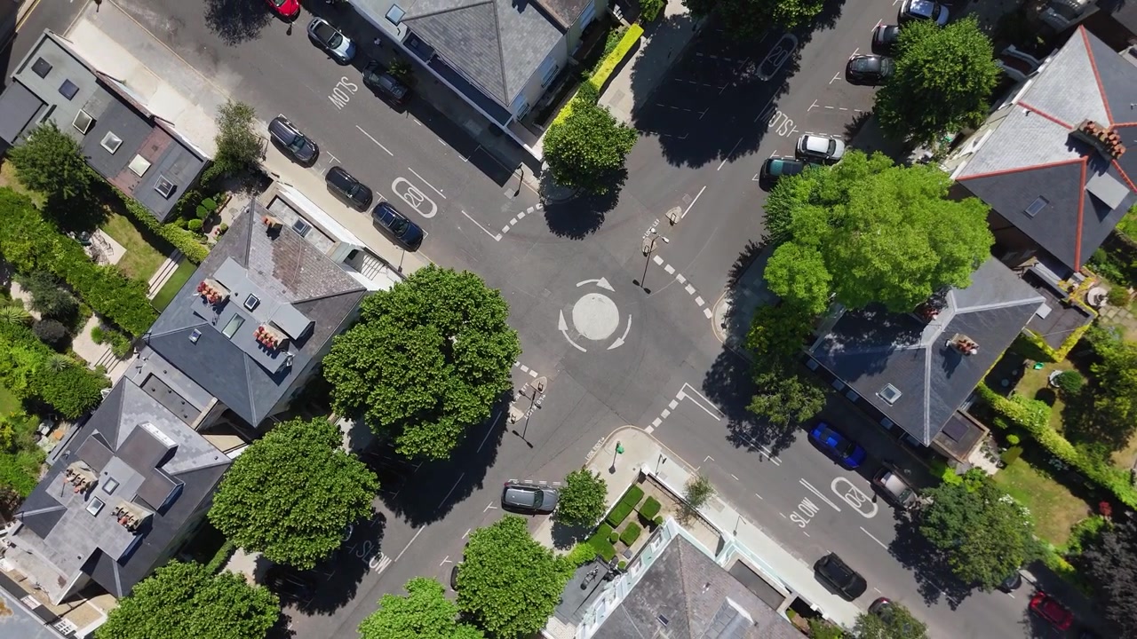 Top down view of a mini roundabout junction shaded by mature street trees in a quiet prime residential neighbourhood