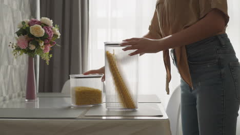 Housewife-stacks-containers-with-spaghetti-on-kitchen-table