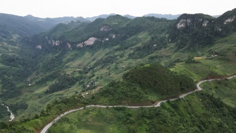 drone flies around a windy mountain pass with a green mountain range at background in ha giang viet nam