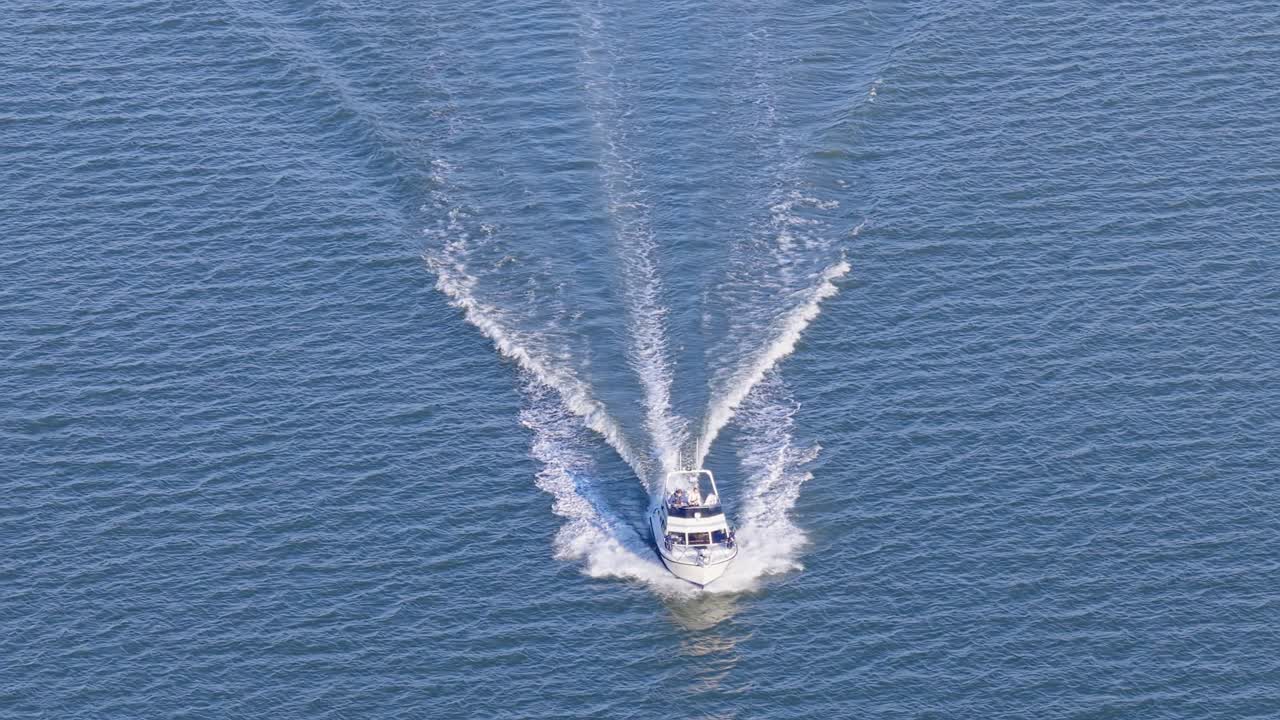 Small leisure motorboat or yacht making way ahead at high speed in calm seas. High altitude aerial drone view from ahead