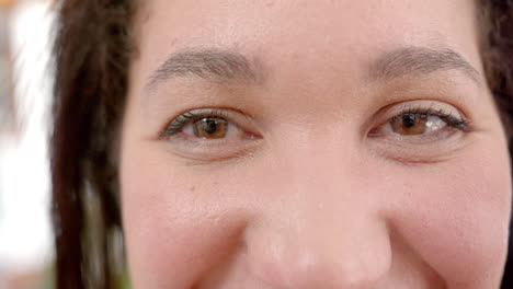 Eyes-of-happy-biracial-woman-with-straight-hair-standing-and-smiling-in-sunny-kitchen