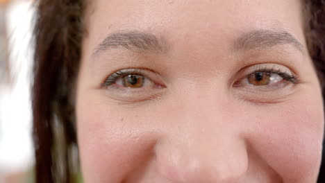 ojos de feliz mujer biracial con el cabello liso de pie y sonriendo en la cocina soleada