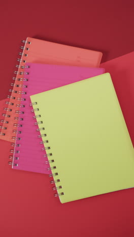 vertical video of overhead view of colourful notebooks on red background, in slow motion