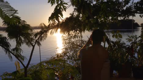 turista filmando el atardecer y el amanecer en un paisaje tropical, el sol naciendo sobre el agua del lago