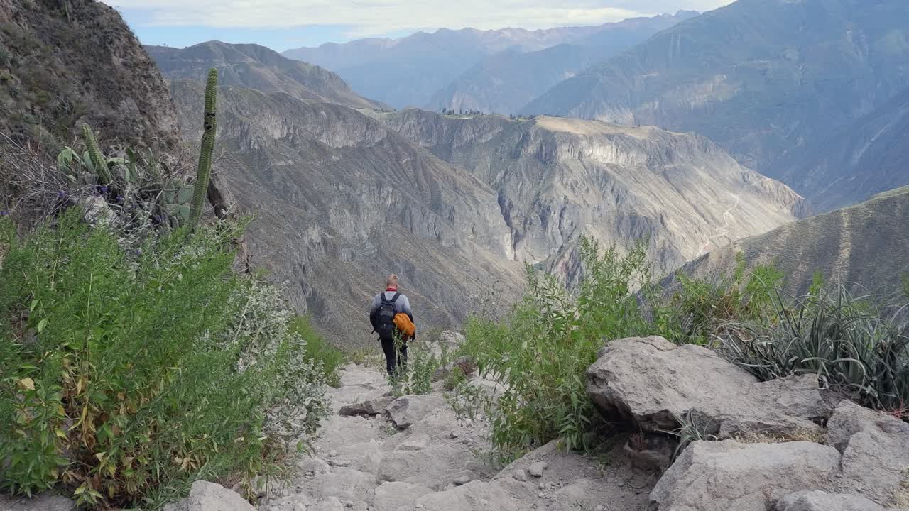 Caucasian man hikes down steep mountain trail, valley bottom far below