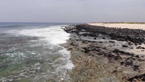 Vuelo-Bajo-Aéreo-Sobre-Olas-Poco-Profundas-Que-Golpean-La-Playa-Rocosa-En-Cabo-Verde