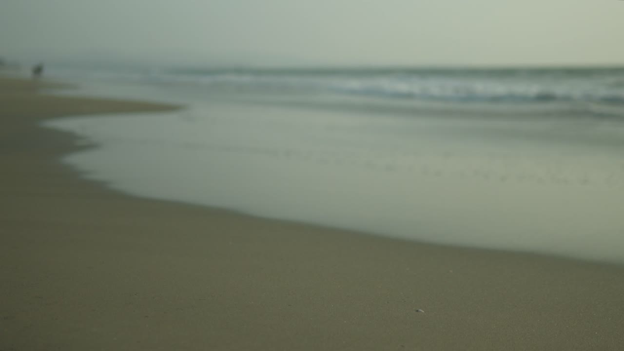 Misty beach scene with soft waves and a solitary figure in the distance, evoking a sense of calm, shot in soft focus