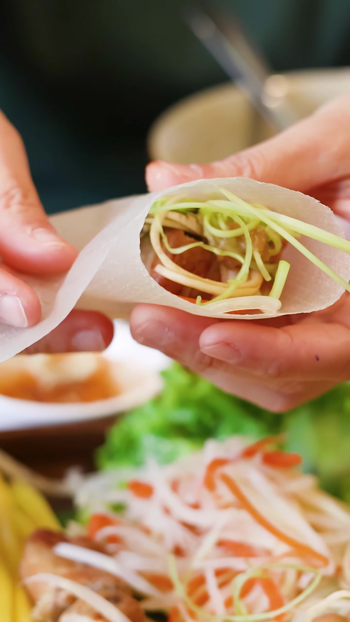 Tangan dengan hati-hati membungkus sayuran segar dan daging babi panggang dalam kertas beras untuk masakan Vietnam.