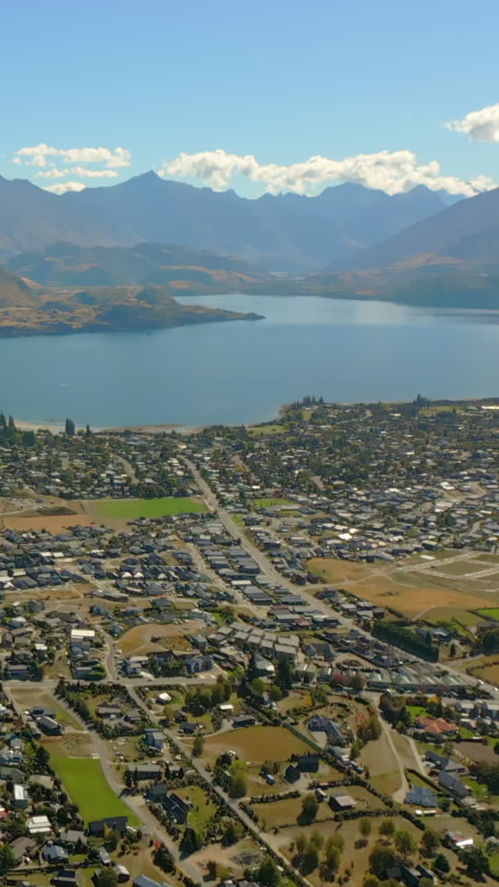 Wānaka village town community - vertical aerial tilt up to reveal Lake Wanaka and the Remarkables Mountain Range