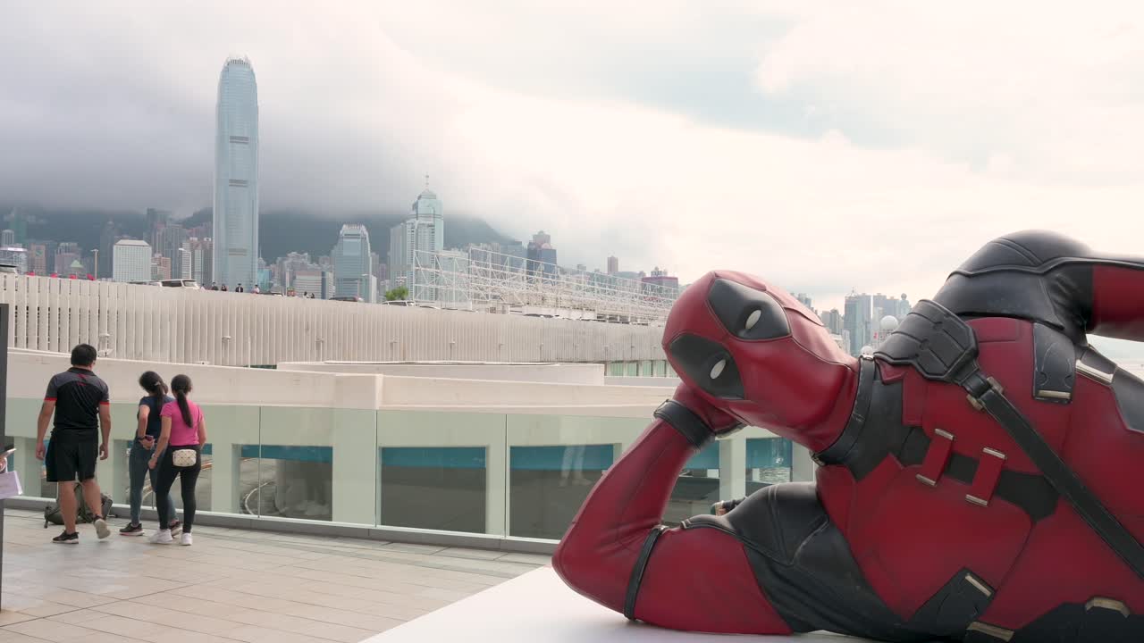 The 8-meter Deadpool installation, promoting Disney's "Deadpool and Wolverine" movie, draws locals and tourists in Hong Kong, with the city skyline in the background.