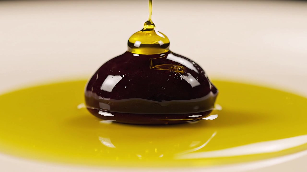 Olio d'oliva dorato versato su un'oliva scura matura