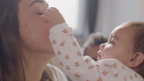 adorable bebé en pijama jugando con su madre en la cama, tocándose y mordiéndose la nariz el domingo por la mañana