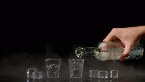 Two-hands-with-glasses-of-vodka-making-cheers,-raising-toast-on-black-background-with-ice-cubes