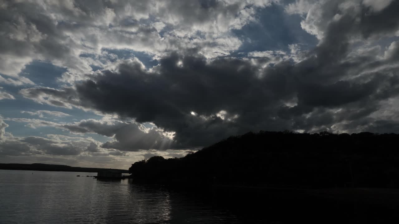 4k 타임 스 태양이 호수와 작은 산 위에 서서 푸른 하늘에 여러 구름을 가지고 있습니다.