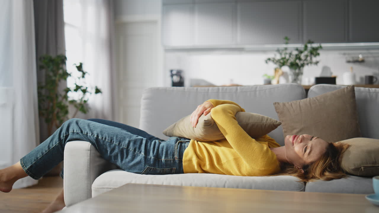 Chilling lady laying sofa embracing pillow at home. Smiling girl feeling relaxed