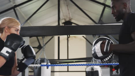 male boxing coach with female boxer in gym using training gloves sparring in ring