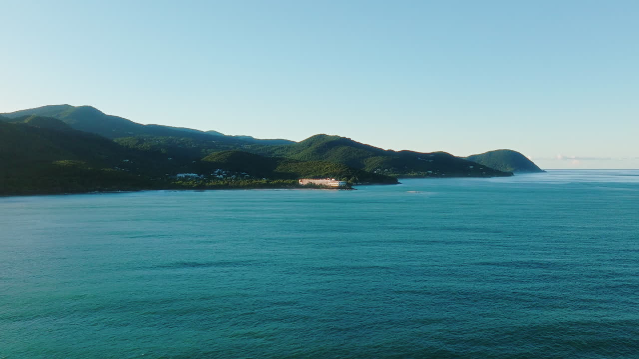 Aerial drone moving over calm sea toward sunlit coastal hotel in Guadeloupe