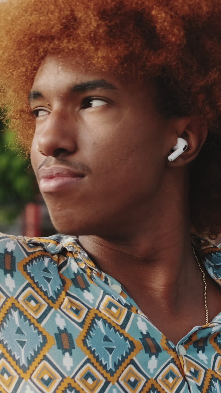 Primo piano di giovane uomo con i capelli ricci e auricolari wireless