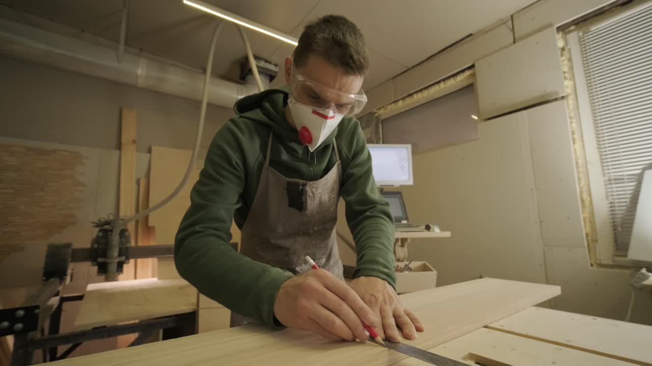 Hardworking professional carpenter in mask and glasses holding a ruler