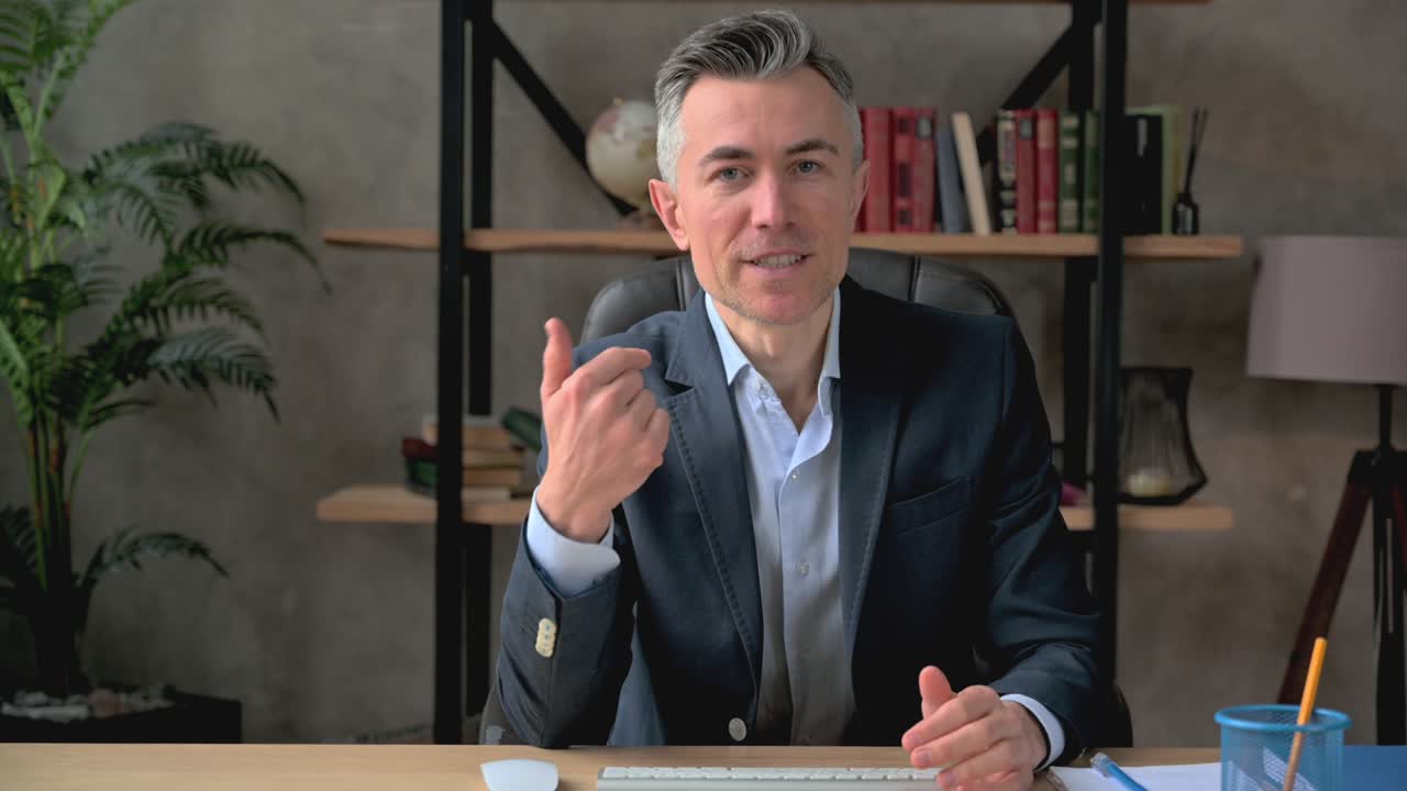 videoconferencia en línea con exitoso inteligente hombre de negocios caucásico de cabello gris, gerente, abogado, que habla por llamada de video, mira a la cámara web, saluda al interlocutor, agita la mano y sonríe amistosamente