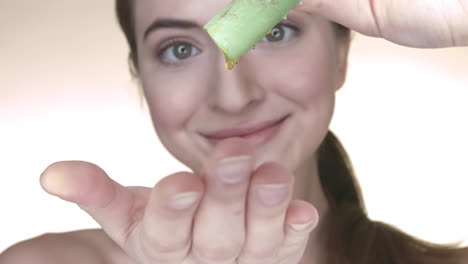 happy young woman squeezes juice of a fresh aloe vera on her hand to make natural cosmetics out of it