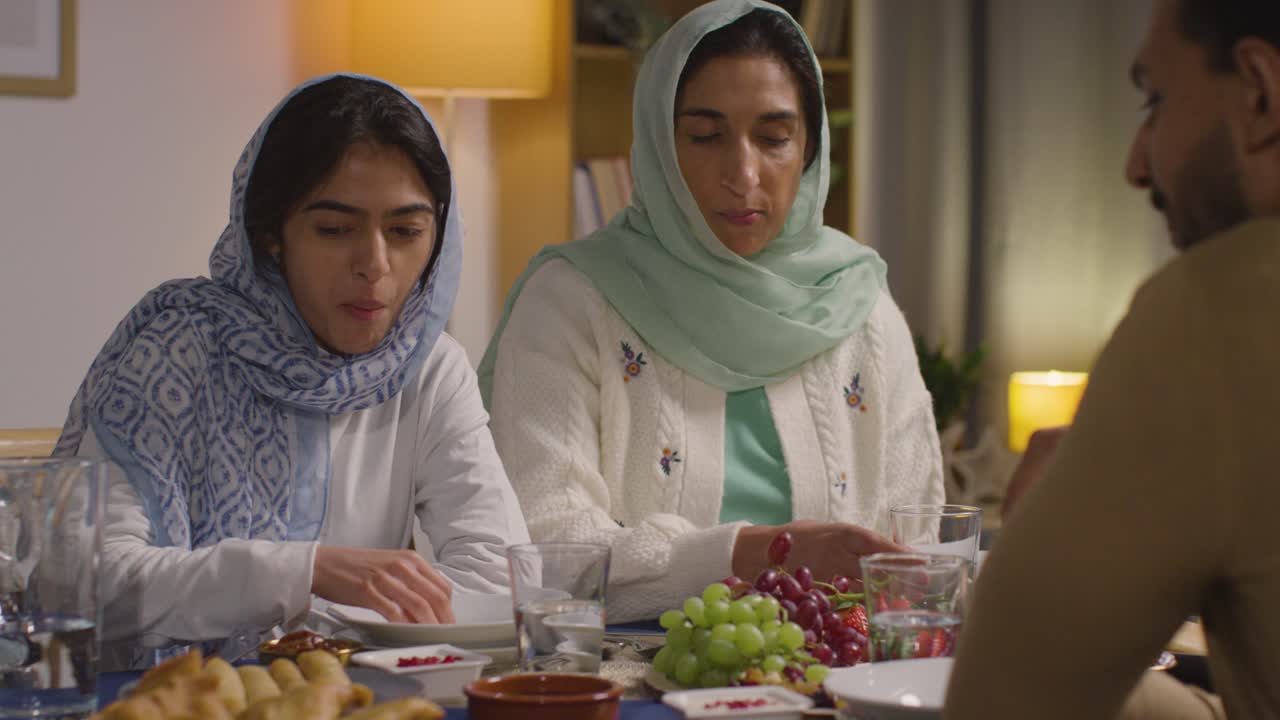 familia musulmana sentada alrededor de una mesa en casa comiendo juntos