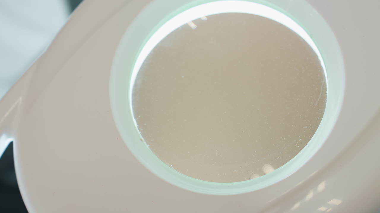 Close-up view of upper section of white magnifying lamp featuring round glass lens with soft illumination and reflective surface, capturing minimalistic and clean salon or workspace environment