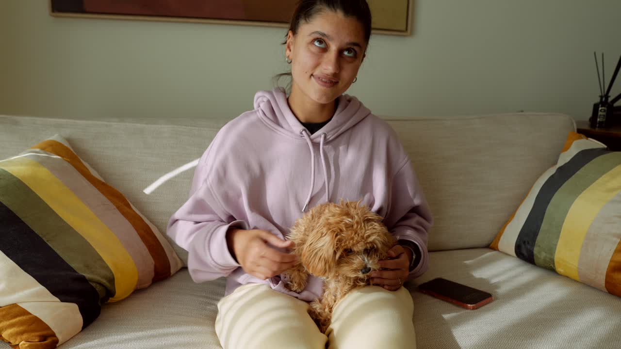 Junge Frau kuschelt und streichelt ihren kleinen Hund auf einem Sofa zu Hause
