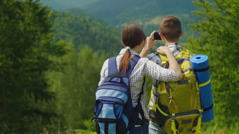 un par de viajeros con mochilas toman fotos de un hermoso paisaje montañoso vacaciones activas