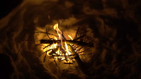 person adding logs to a fire in a hole in the snow during a cold winter night in the alps