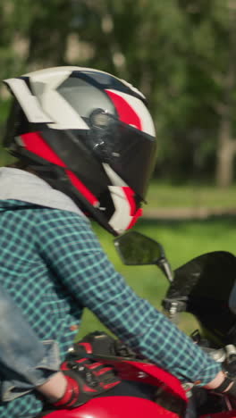 two friends are riding a red power bike with helmets on, traveling along a road with blurred green trees and a metal signpost in the background