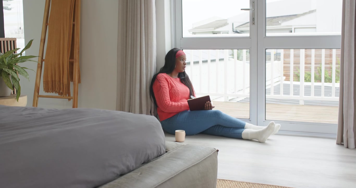 Light drawing gaze, African American woman sitting on floor holding tablet, looking out, copy space